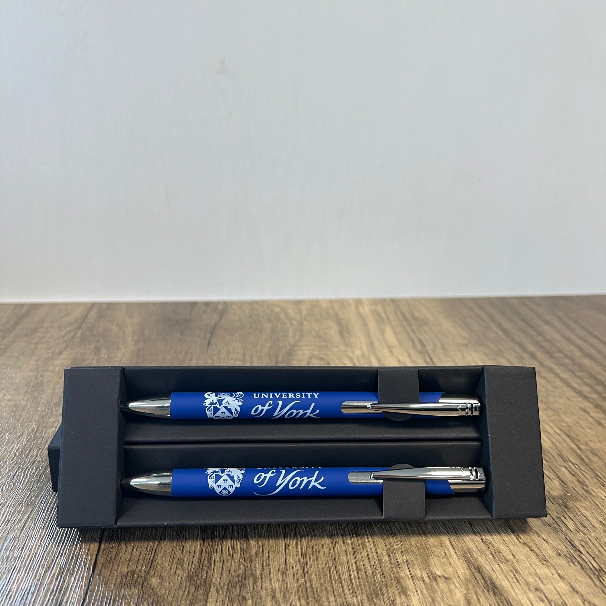 Two blue pens with silver accents in a black holder on a wooden surface.
