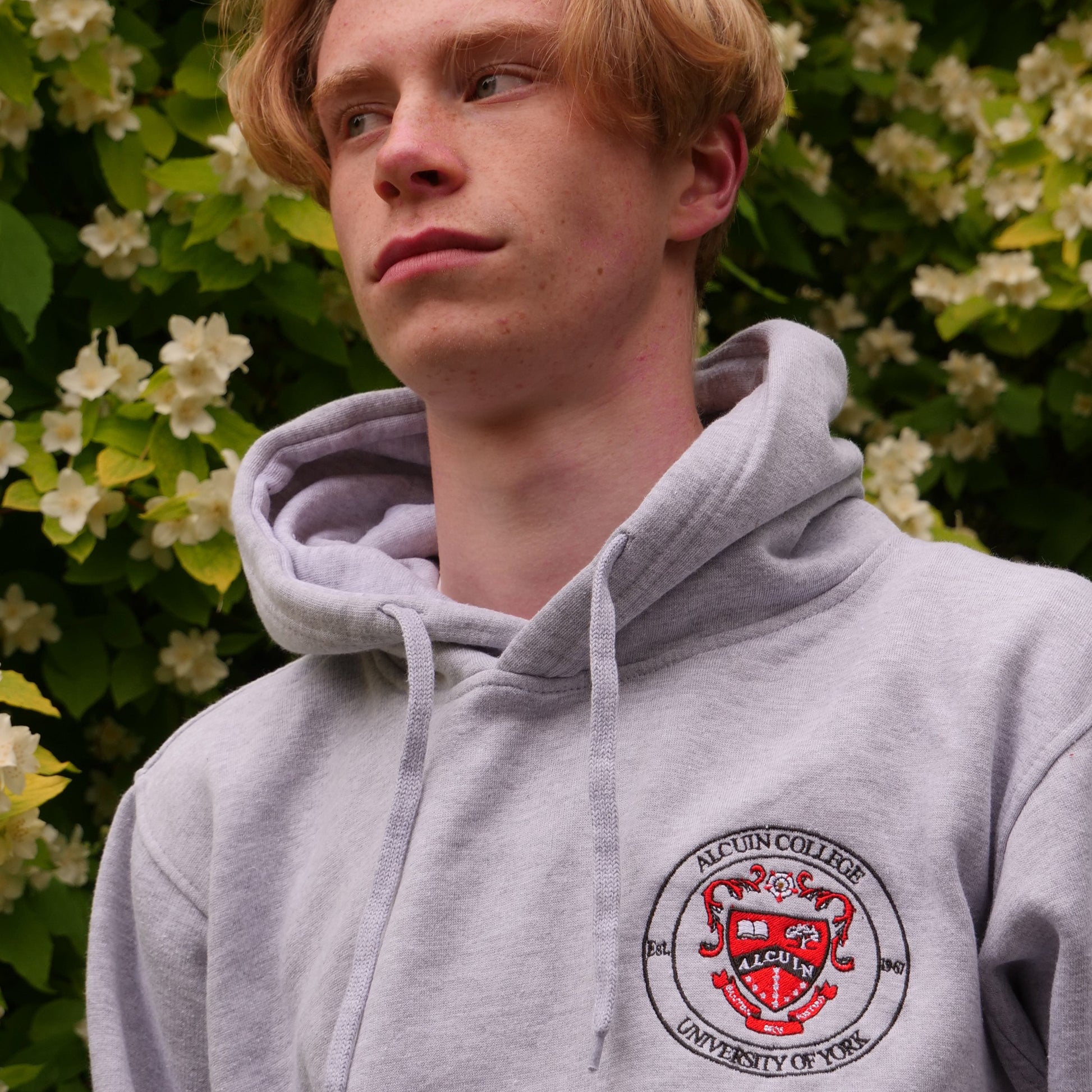Person wearing a gray hoodie with a logo, standing among flowers