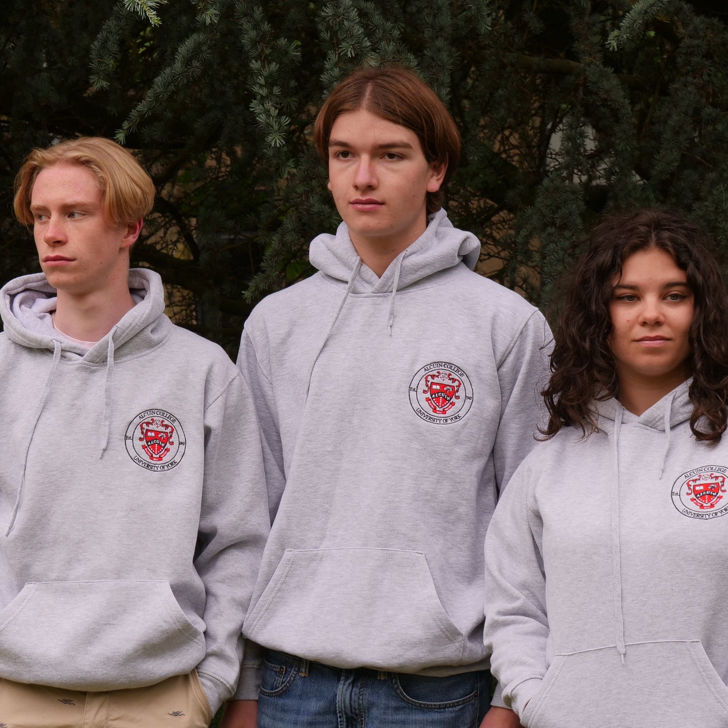 Three people wearing gray hoodies with a logo outdoors.