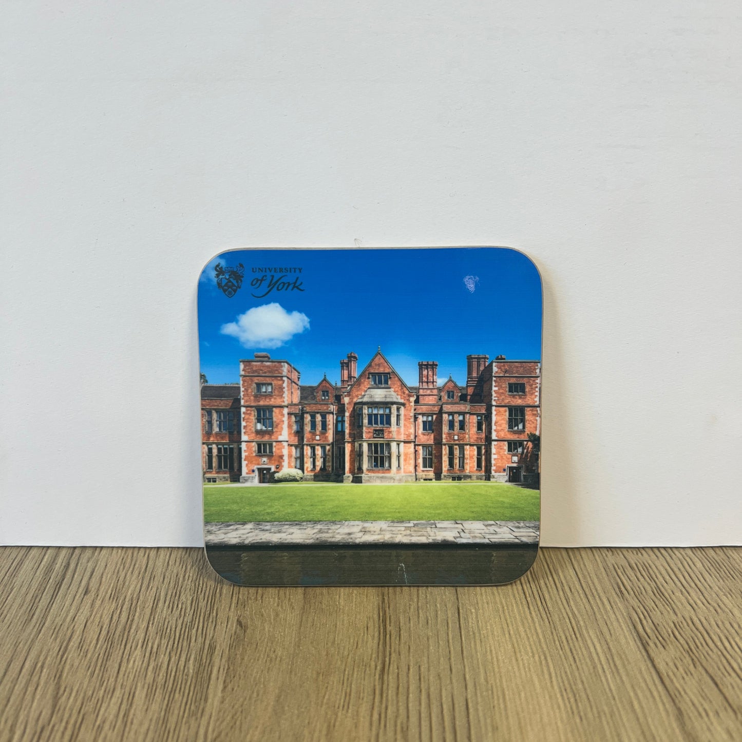 Coaster with a printed design of a building on a white surface with a wooden edge.